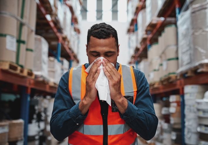 The image shows a man in a safety vest blowing his nose as the featured image for Managing Allergies in the Workplace